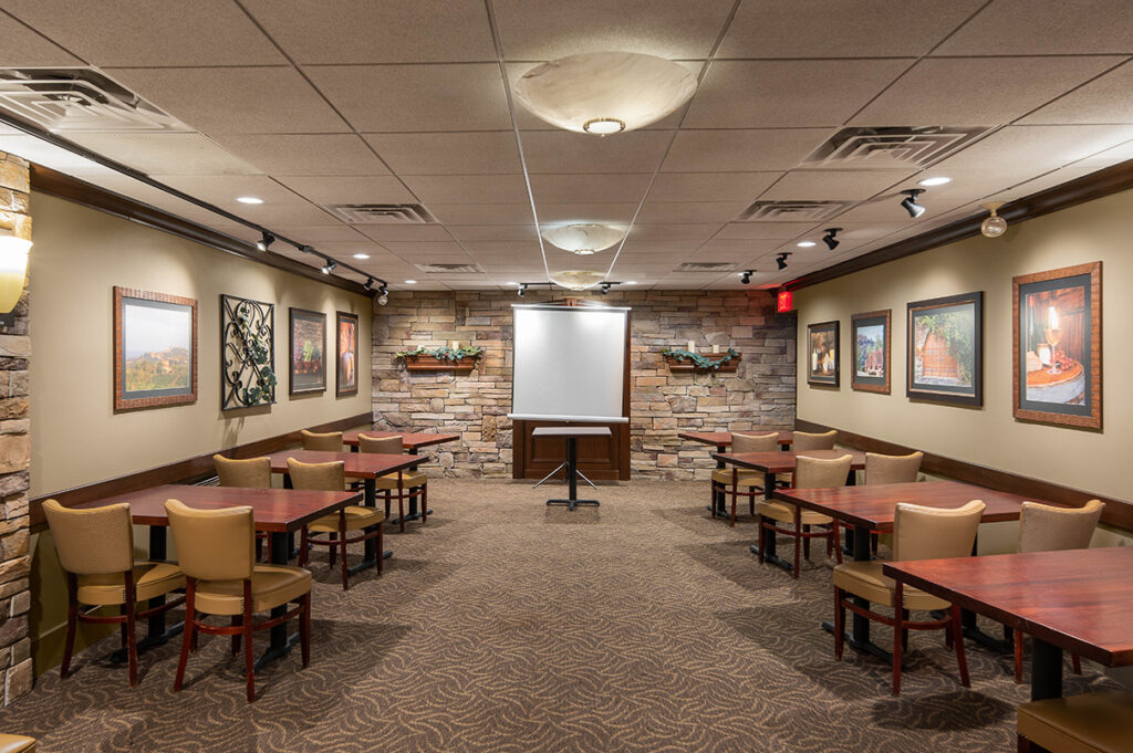 Private dining room with stone accent wall, framed artwork, tables and chairs, and a projector screen for events.