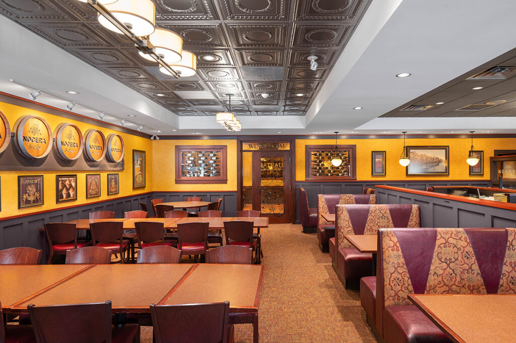 Elegant dining room with warm lighting, patterned ceiling, booth seating, and wine displays at The Chateau restaurant.