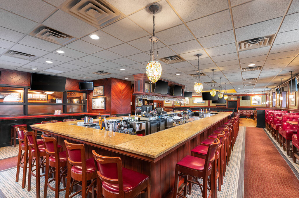 Spacious restaurant bar with granite countertop, red bar stools, warm lighting, and classic wood interior.