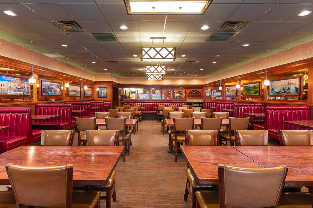 Spacious restaurant dining room with wooden tables, red leather booths, framed wall art, and warm overhead lighting.
