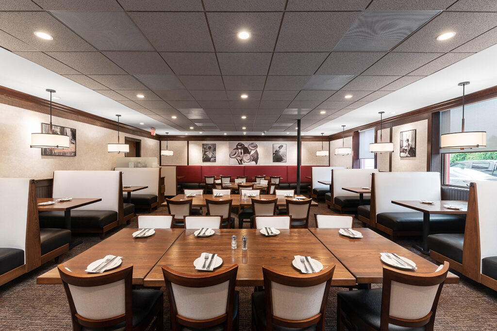 Spacious restaurant dining area with booth seating, wooden tables set with plates, and modern pendant lighting.