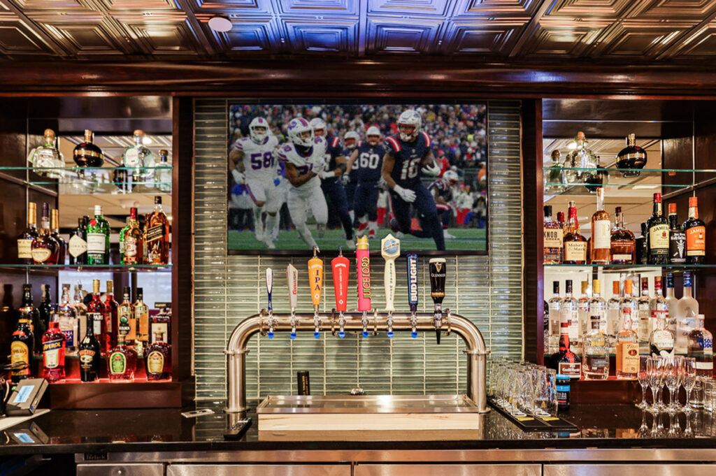 Fully stocked restaurant bar with beer taps, liquor shelves, and a large TV showing a football game.