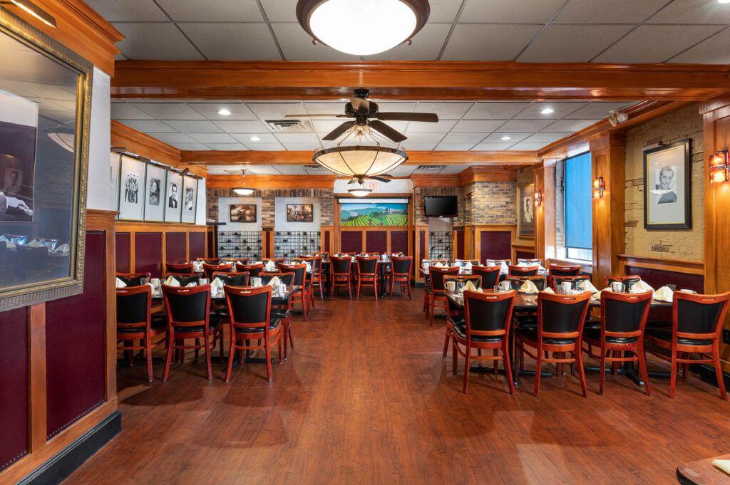 Elegant restaurant dining room with wooden floors, neatly set tables, framed photos, and warm lighting in a classic interior.