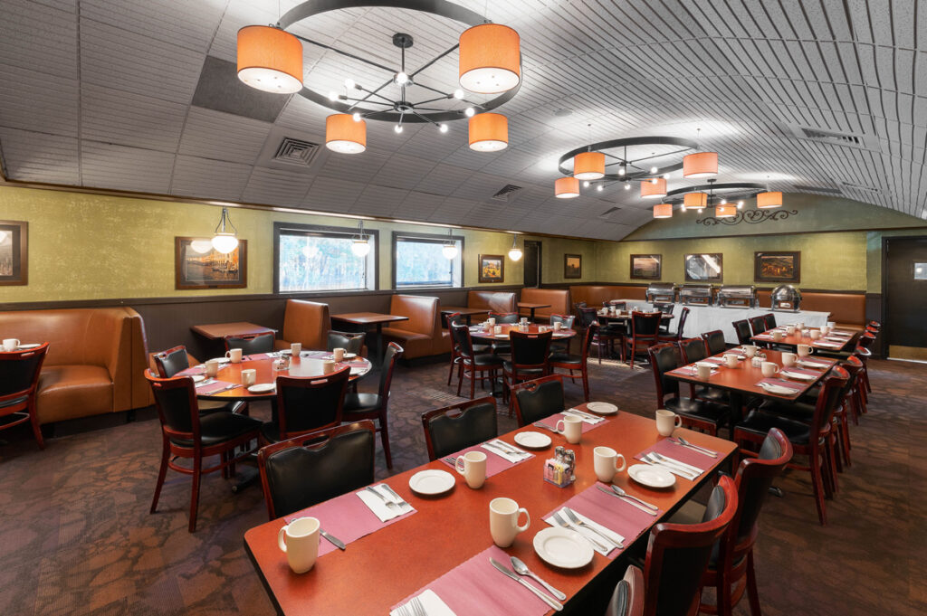 Spacious restaurant dining room with booth seating, set tables, warm lighting, and buffet area at The Chateau.