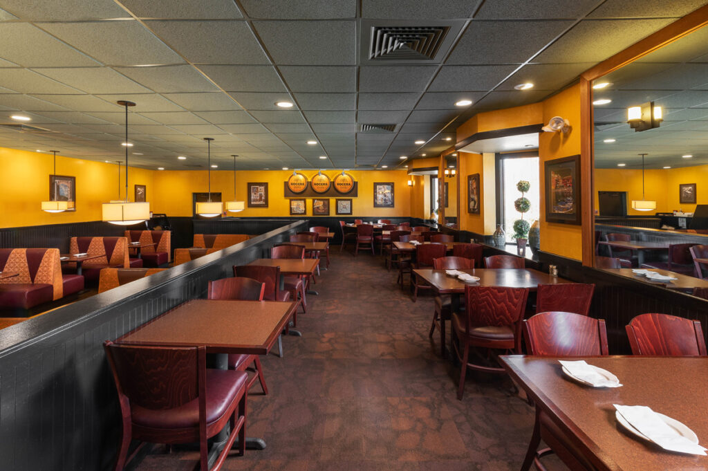 Warmly lit restaurant dining area with booths and tables, yellow walls, framed art, and comfortable seating at The Chateau.