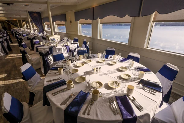 Spacious banquet hall with round tables, white linens, navy chair sashes, hardwood dance floor, and bar area.